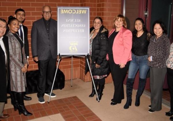 Nine alumni volunteers smiling and posing next to a poster that reads "Welcone alumni association reception March 24, 2023"